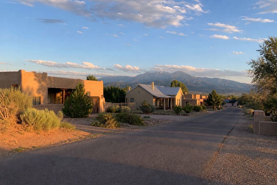 Earth-tone stucco homes along a Northern New Mexico street with mountains behind
